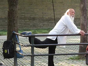 A man with long white beard stretching on the ground.