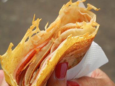 A person holding a tortilla with cheese and meat.